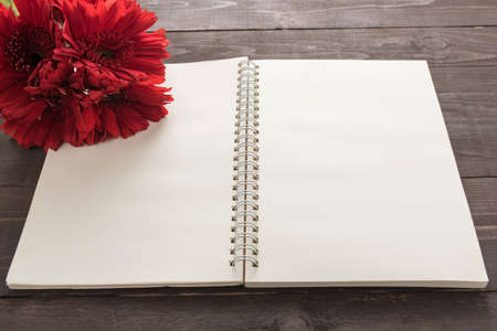Red gerbera flowers and notebook are in the wooden background.の写真素材