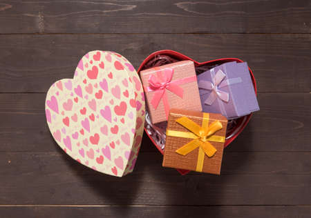 Gift boxes are in heart box, on the wooden background with empty space.
