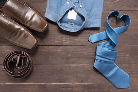 Elegant set: brown men's shoes, brown leather belt, blue shirt, blue necktie, on the wooden background.の写真素材