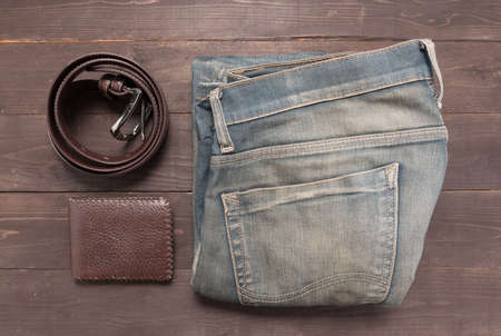 Elegant set: brown wallet, jeans and brown leather belt, on the wooden background.