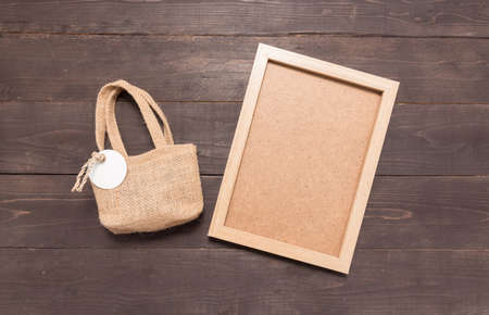 Hessian sack bag with tag and picture frame are on the wooden background .の写真素材
