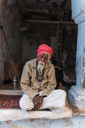 An old Indian man with a red turban and beard sitting in front of his house in Pushkar, Indiaのeditorial素材