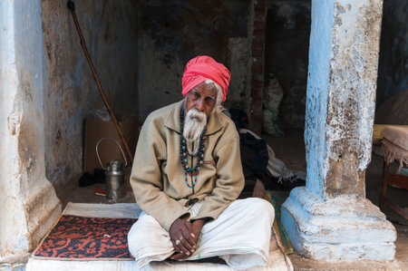 An old Indian man with a red turban and beard sitting in front of his house in Pushkar, Indiaのeditorial素材