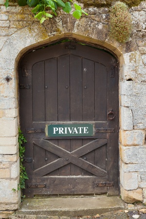 Weathered exterior door set in a buff coloured stone wall  Door has Private sign の写真素材