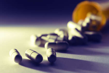 Pills spilling out of a tipped over pill bottleの写真素材