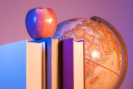 Apple placed on a stack of books in front of an antique earth globe. の写真素材