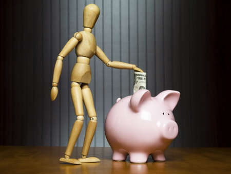 Manikin dropping a dollar into a piggy bank