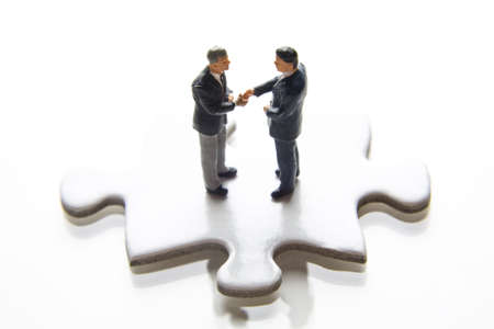 Businessman figurines shaking hands while standing on a puzzle pieceの写真素材