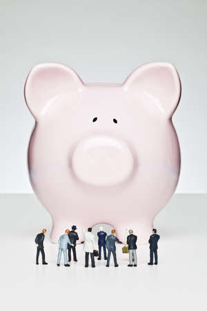 Business figurines placed in front of a pink piggy bankの写真素材