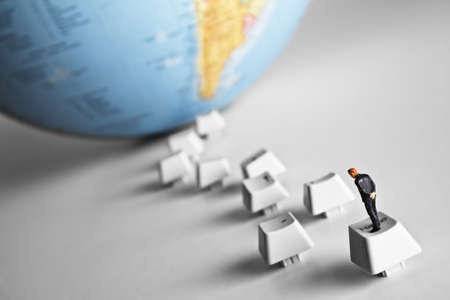Business figurine placed on computer keys that lead to an earth globeの写真素材
