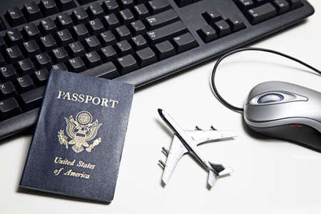 Computer mouse, toy airplane, passport and keyboard placed on a white tabletop. の写真素材
