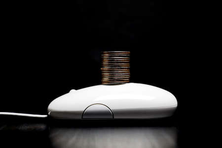 White computer mouse with stack of coins placed on topの写真素材