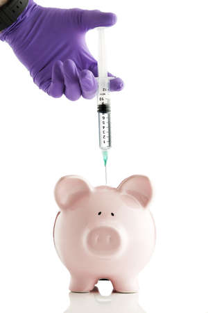 Gloved hand holding syringe over a piggy bank.  の写真素材