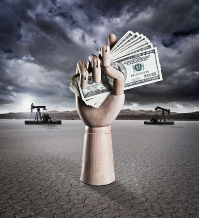 Manikin hand holding money in dry lake bed with storm clouds and drilling rigs in backgroundの写真素材