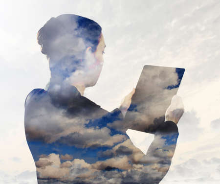 Woman with digital tablet composited with images of cloudsの写真素材