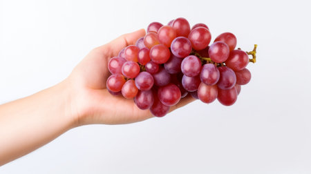 a hand holding a bunch of ripe red grapes, highlighting their plumpness and freshness against a white backdrop. AI generatedの素材