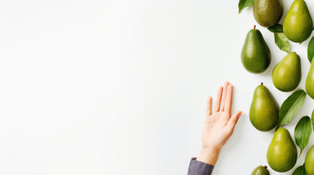 A hand reaches toward fresh, ripe avocados arranged on a clean white surface, highlighting a healthy lifestyle and vibrant food choices. Ideal for culinary themes.の素材