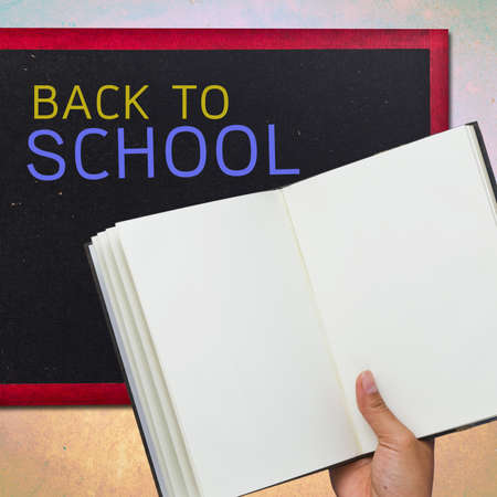 Hand holding the opened notebook with Back To School text on blackboardの写真素材
