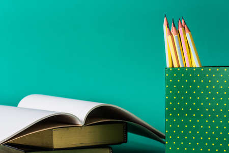 Pencils in cardboard box with opened notebook on green background
