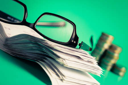 Eyeglasses with pile of bills and coins on green backgroundの写真素材