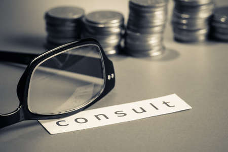 Financial consultant, eyeglasses and coins with paper of consult wordの写真素材