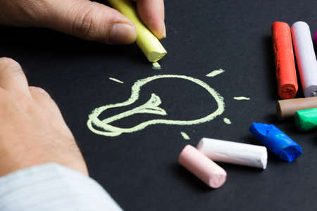 Hand drawing light bulb on black paper with pastel chalkの写真素材