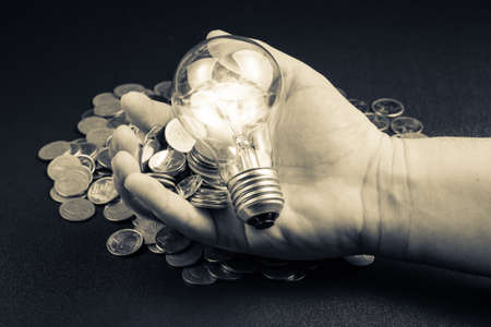 Coins and light bulb in hand as concept of financial plan or smart investmentの写真素材