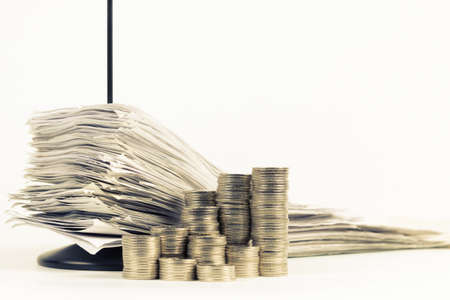 Stack of receipts in paper nail with heap of coins on white backgroundの写真素材