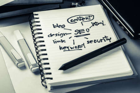 SEO concept and topic, handwritten in notebook with part of laptop, pen, and book on the deskの写真素材