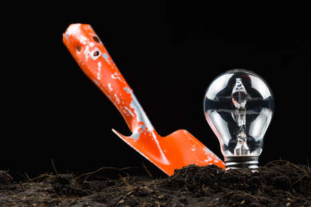 Light bulb as idea symbol in soil with shovel to digの写真素材