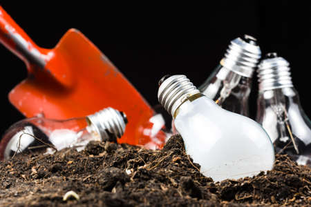 Many light bulbs as ideas in soil with shovel to dig and collectの写真素材