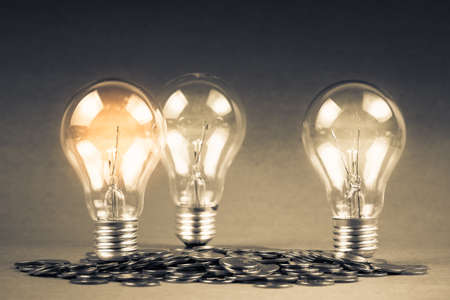 Glowing light bulbs and pile of coinsの写真素材