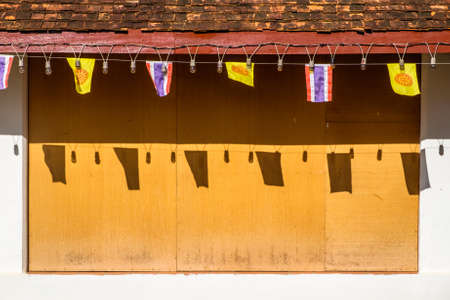 Abstract wall and roof of traditional Thai temple with decorated light bulbs and flagsの写真素材