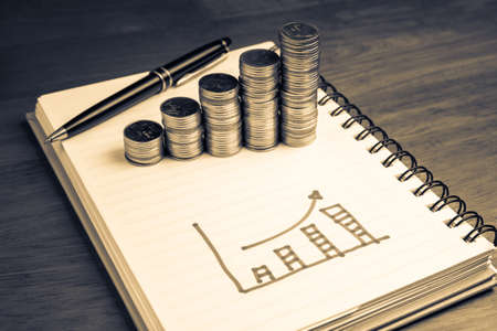 Drawing growth graph in notebook with heap coins stair, financial plan concept