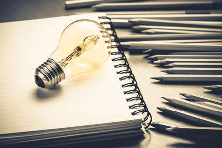 Glowing light bulb with pencils and notebook on wood table