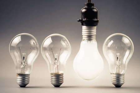 Hanged light bulb glowing from above with other light bulbs that look similar but not sparkle on the groundの写真素材