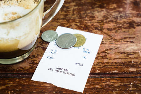 Closeup coffee receipt and coin tip on wood tableの写真素材