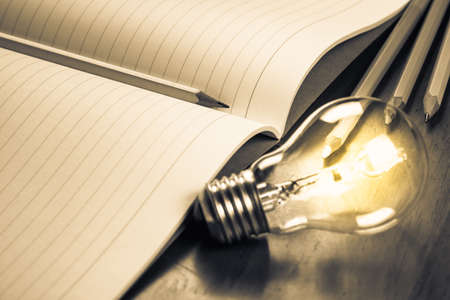 Closeup pencil on opened notebook with glowing light bulb, creative writing conceptの写真素材