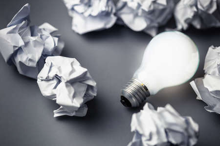 Light bulb glowing among crumpled papers on the groundの写真素材