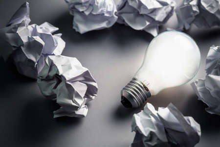 Light bulb glowing among crumpled papers on the groundの写真素材