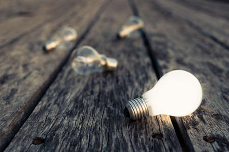 White light bulb glowing on wood plank, different from othersの写真素材