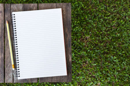 Opened notebook on wood table and green grasses