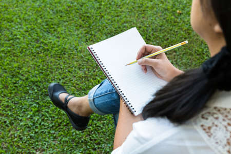 Closeup woman in the park thinking to write something with blank notebook placed on her lapの写真素材