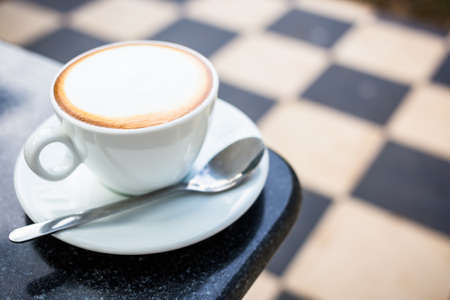 Cup of cappuccino at the table corner on blurred tiled floor backgroundの写真素材