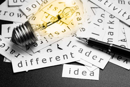 Pile of inspiration words printed in pieces of paper with light bulb and pen, closeup at Different...