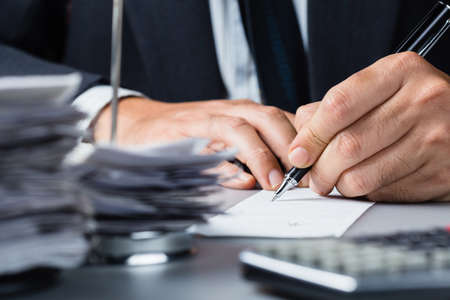 Businessman writing on bill with pile of bills in paper nail