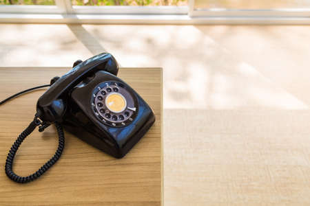 Old analog telephone on the desk with sunlight through the glass doorの写真素材