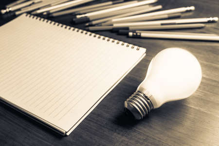 Creative Writing, glowing light bulb on the table with notebook and many pencilsの写真素材