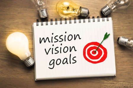 Mission Vision Goals text on notebook with drawing accurate target and light bulbs aroundの写真素材
