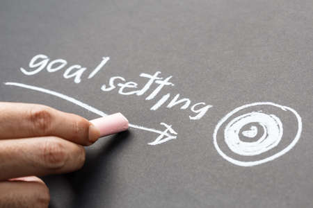 Closeup hand writing text Goal Setting with drawing arrow and target on chalkboardの写真素材